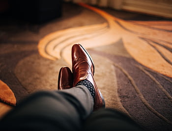 Close-up of polished brown leather shoes worn with patterned socks, relaxed indoors. HD wallpaper