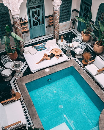 Elegant indoor pool with a woman lounging, set within a Moroccan riad in Marrakesh. HD phone wallpaper
