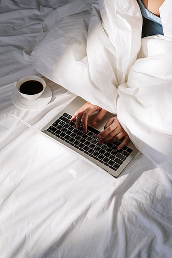 Comfortable home office setup with a laptop on bed and a cup of coffee, perfect for remote work. HD phone wallpaper