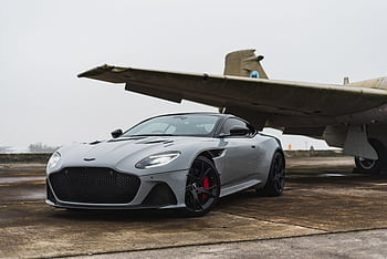 Sleek grey luxury car parked beneath an old aircraft on a foggy day. HD wallpaper