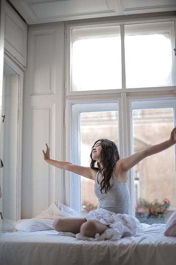 A woman enjoys the morning sunlight as she stretches in bed, feeling relaxed and refreshed. HD phone wallpaper
