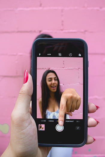 A woman captures her selfie using a smart against a vibrant pink wall. HD phone wallpaper
