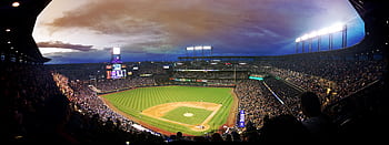 Wide-angle view of a baseball stadium at dusk capturing the field and excited crowd. HD wallpaper