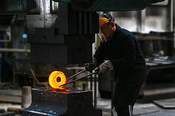 A blacksmith skillfully working with red-hot metal in an industrial setting, showcasing craftsmanship. HD wallpaper