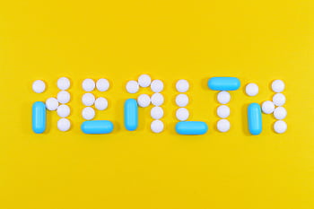 Pills spelling 'health' on a vibrant yellow background, symbolizing wellness. HD wallpaper