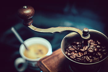 Close-up of a vintage coffee grinder with fresh coffee beans next to a steaming cup. HD wallpaper