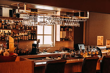 A stylish bar interior featuring hanging glassware, a range of spirits, and wooden furnishings. HD wallpaper