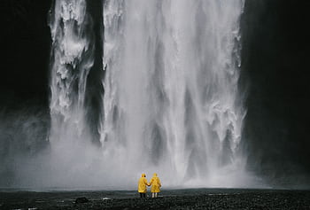 Couple in yellow raincoats standing before a magnificent waterfall, capturing a moment of adventure and romance. HD wallpaper