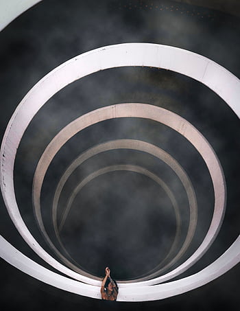 A dramatic top-down view of a spiral staircase enveloped in smoke, showcasing modern architectural style. HD phone wallpaper