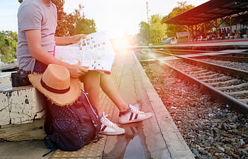 Person sitting at train station platform reading map, embracing travel adventure. HD wallpaper