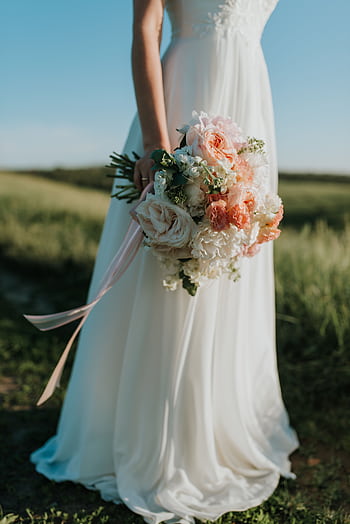 A bride in a flowing white gown holds a colorful bouquet in a sunny field. HD phone wallpaper