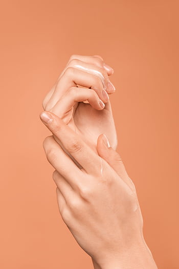 Close-up of hands with oil on peach background, emphasizing skincare and wellness. HD phone wallpaper