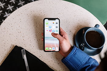 Person interacts with smart and coffee on a terrazzo table, showcasing apps and casual lifestyle. HD wallpaper