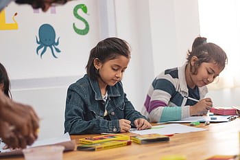 Young girls engaging in creative drawing activities in an Indian classroom setting. HD wallpaper