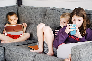 Children relaxing at home using smarts and tablets on a cozy sofa. HD wallpaper