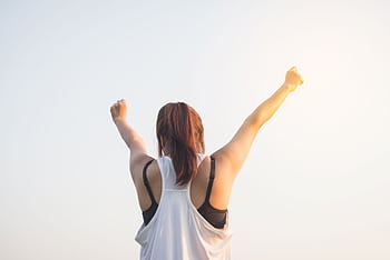 A woman celebrates success with arms raised in a bright outdoor setting. HD wallpaper