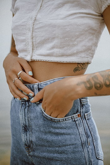 Close-up of a woman's tattooed abdomen wearing a crop top and jeans, showcasing fashion and style. HD phone wallpaper