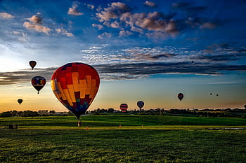 Vibrant hot air balloons take off at dawn over a rural field, showcasing a que landscape. HD wallpaper