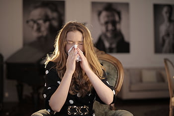 A young woman with closed eyes sneezing into a tissue, sitting indoors. HD wallpaper