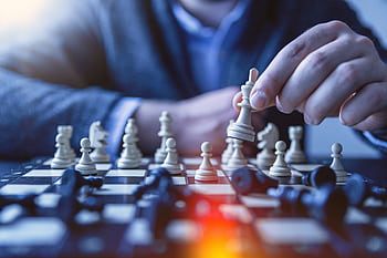 Close-up of a hand making a strategic chess move on a board, emphasizing thought and planning. HD wallpaper