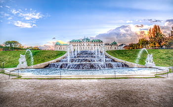 Captivating view of Belvedere Palace with lush gardens and dynamic fountains under a bright sky. HD wallpaper