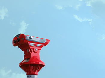 Red sightseeing telescope pointing against a bright blue sky, ideal for travel exploration concepts. HD wallpaper