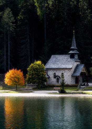 Peaceful stone chapel by a lake in Trentino-South Tyrol with autumn colors reflecting in the water. HD phone wallpaper