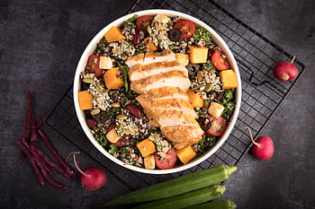 A vibrant bowl of grilled chicken salad with quinoa, fresh vegetables, and seeds. HD wallpaper