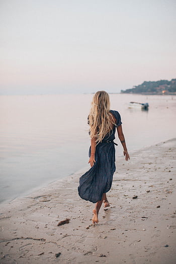 A woman walks barefoot on the seashore at sunset, wearing a blue dress for a serene vacation moment. HD phone wallpaper