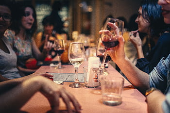A lively scene of friends enjoying wine and conversation in a cozy bar setting. HD wallpaper