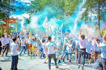 Energetic crowd enjoying a vibrant outdoor festival with colorful powder at daytime. HD wallpaper
