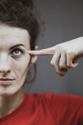 Close-up portrait of a woman in red, pointing to her temple, capturing a thoughtful expression. HD phone wallpaper