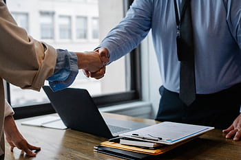 Two business professionals shaking hands in a modern office setting, symbolizing successful collaboration. HD wallpaper