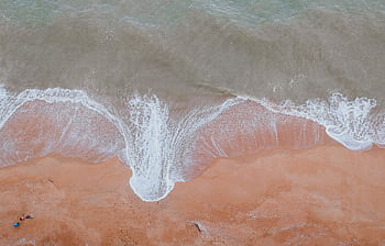 Captivating aerial view of ocean waves gently washing over a sandy beach, perfect for travel and nature themes. HD wallpaper
