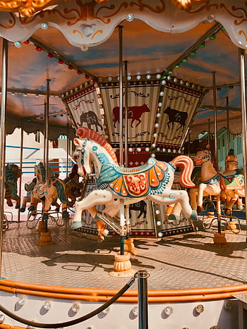 A vibrant carousel with ornate horses at a theme park in Thailand during daylight. HD phone wallpaper