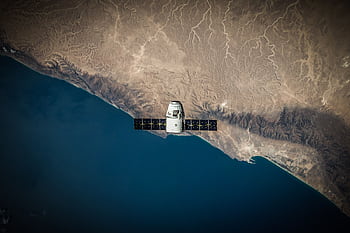 A satellite hovering above Earth's coastline, captured from space. HD wallpaper