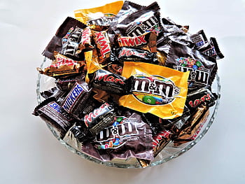 A bowl filled with various chocolate candies, including Twix, Snickers, and M&Ms, creating a vibrant dessert spread. HD wallpaper