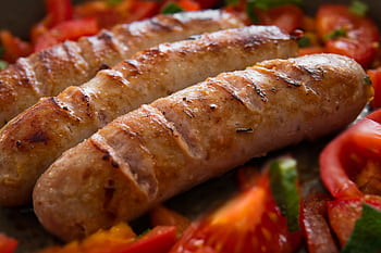 Close-up of juicy grilled sausages served with fresh sliced tomatoes. HD wallpaper