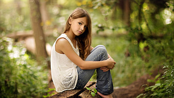 Cute Little Girl Is Sitting On Wood Wearing White Top And Blue Jeans In Blur Bokeh Background Cute HD wallpaper