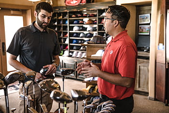 Customer receiving expert advice from salesman on golf equipment in a store. HD wallpaper