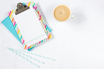 A minimalist flat lay of a colorful notepad, coffee cup, and pencils on a white desk, ideal for creative work. HD wallpaper