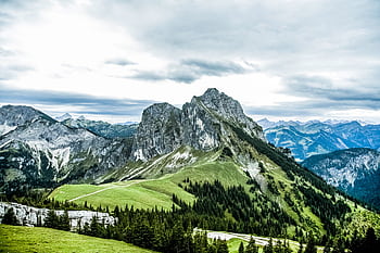 Breathtaking view of rugged mountains and lush green fields under a cloudy sky. Ideal for nature enthusiasts. HD wallpaper