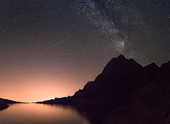 A captivating view of the Milky Way and shooting star above a silhouetted mountain reflecting over a calm lake. HD wallpaper