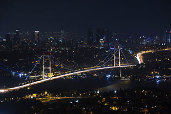 Capture of the iconic Bosphorus Bridge lit up against Istanbul's vibrant cityscape at night. HD wallpaper
