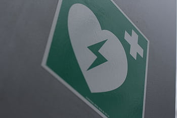 Green first aid sign featuring a broken heart and cross symbol for medical emergency awareness. HD wallpaper