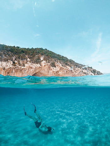 A serene over-under graph capturing a diver exploring the turquoise waters off the coast of Sardinia, Italy. HD phone wallpaper