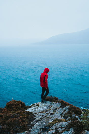 Lone person in red jacket on a foggy cliff in the UK, overlooking the ocean. HD phone wallpaper