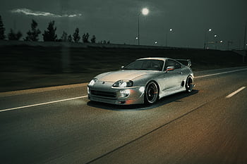 A luxurious silver sports car swiftly moves down a nighttime road, headlights illuminating the way. HD wallpaper