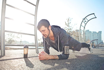 A young man performs a plank exercise outdoors with ears, a , and a water bottle nearby. HD wallpaper