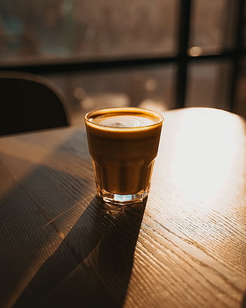 A cozy cappuccino glows in the warm sunset light on a wooden table, inviting relaxation. HD phone wallpaper